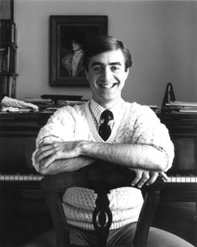 David Earl seated on a chair at the piano and smiling at the camera
